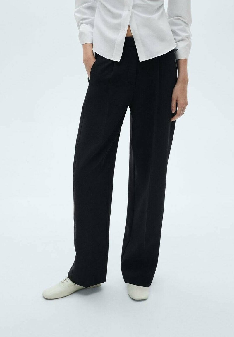 Pantalon noir à jambes larges avec une texture lisse, présentant des plis devant, des poches latérales, et une taille haute, associé à une chemise blanche boutonnée.