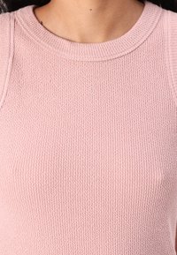 Helles rosa strukturiertes Oberteil mit einem gerippten Muster, ausgestattet mit einem runden Ausschnitt und ärmellosem Design, aus weichem, gewebtem Material gefertigt.