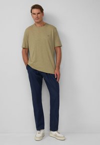 Oliwkowa koszulka z krótkim rękawem o subtelnej fakturze, zestawiona z granatowymi spodniami i białymi trampkami, z jasnymi akcentami.