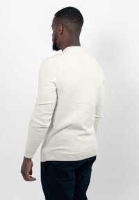 Witte gebreide trui met lange mouwen en een ronde hals, zachte textuur, aansluitend ontwerp, gecombineerd met donkere broeken. Zicht van achteren.
