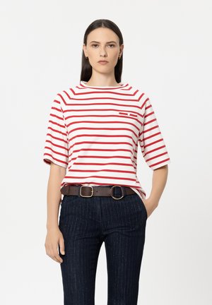 Red and white striped short-sleeve shirt with a high neckline, featuring a small pocket detail. Worn with navy pinstriped pants and a brown belt.