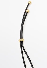Fili in pelle nera con perle in metallo dorato e un pezzo d'accento incisa, caratterizzati da una texture liscia e un design elegante.