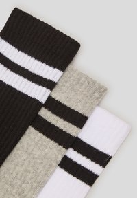 Tre paia di calze da crew in nero, grigio e bianco, ciascuna con texture a coste e due righe orizzontali vicino alla parte superiore.