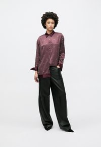 Camicia in seta a righe borgogna con scollo con colletto e chiusura frontale con bottoni, abbinata a pantaloni neri a gamba larga.