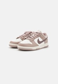 Nike Dunk Low sneakers med en lys brun skinnøvre, hvit tåboks og beige detaljer, med en avrundet form og teksturerte såler.