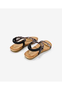 Sandalias trenzadas negras con suela de corcho y plantilla color marrón. Las correas tienen una textura tejida en una mezcla de colores negros y patrones.