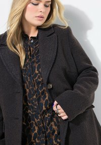 Donkerbruine geweven wollen jas met inkepingen en een enkele knop. Draag het over een blouse met luipaardprint in donkere blauwtinten en bruine tonen.
