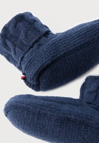 Ζευγάρι σκούρων μπλε πλεκτών γαντιών με υφασμάτινα μοτίβα, ριγωτές μανσέτες και μια μικρή υφασμάτινη ετικέτα σε κόκκινο, λευκό και μαύρο σε ένα γάντι.