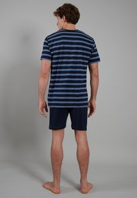 Himmelblau und marineblau gestreiftes Kurzarmhemd, kombiniert mit marinen Shorts. Weicher Stoff, lässiger Schnitt und sichtbare Nähdetails.