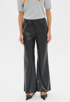 Black faux leather wide-leg pants with an elastic waistband. Smooth texture and flowing design. Styled with a gray short-sleeve top.