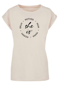 Lys pink kortærmet t-shirt med rund halsudskæring, der prydes af et cirkulært sort tekstdesign med ord relateret til moderskab.