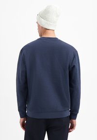 Marineblauwe sweatshirt met een textuurafwerking. Heeft lange mouwen, een ronde hals en geribbelde manchetten. Gepaard met een lichtgrijze gebreide beanie.