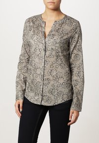 Langærmet bluse i et lyst beige stof med blomstermotiv i mørkegrå. Har en rund halsudskæring og knaplukning foran.