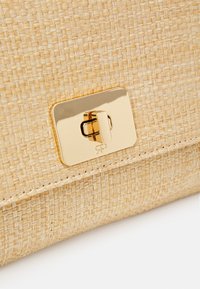 Beige geweven handtas met een gestructureerde afwerking, voorzien van een glanzende gouden sluiting. Het ontwerp heeft een rechthoekige vorm met gedetailleerde stiksels.
