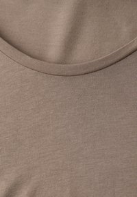 Nærbillede af et strikket beige stof med detalje ved rund halsudskæring.