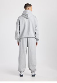 Sweat-shirt gris et pantalon de survêtement assorti en tissu doux. Le sweat à capuche possède un grand col, et le pantalon est équipé de poignets élastiques. Les chaussures sont blanches et grises.