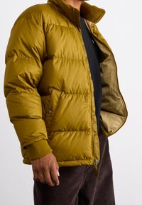 Gul puffjakke med høj krave, lynlåslukning og ribbede manchetter. Tekstureret stof, quiltet design og en blød inderforing.