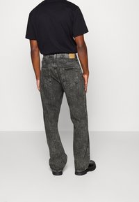 Dark gray denim jeans with a relaxed fit, featuring a small brown leather patch at the waistband and two back pockets. Simple stitching detail.