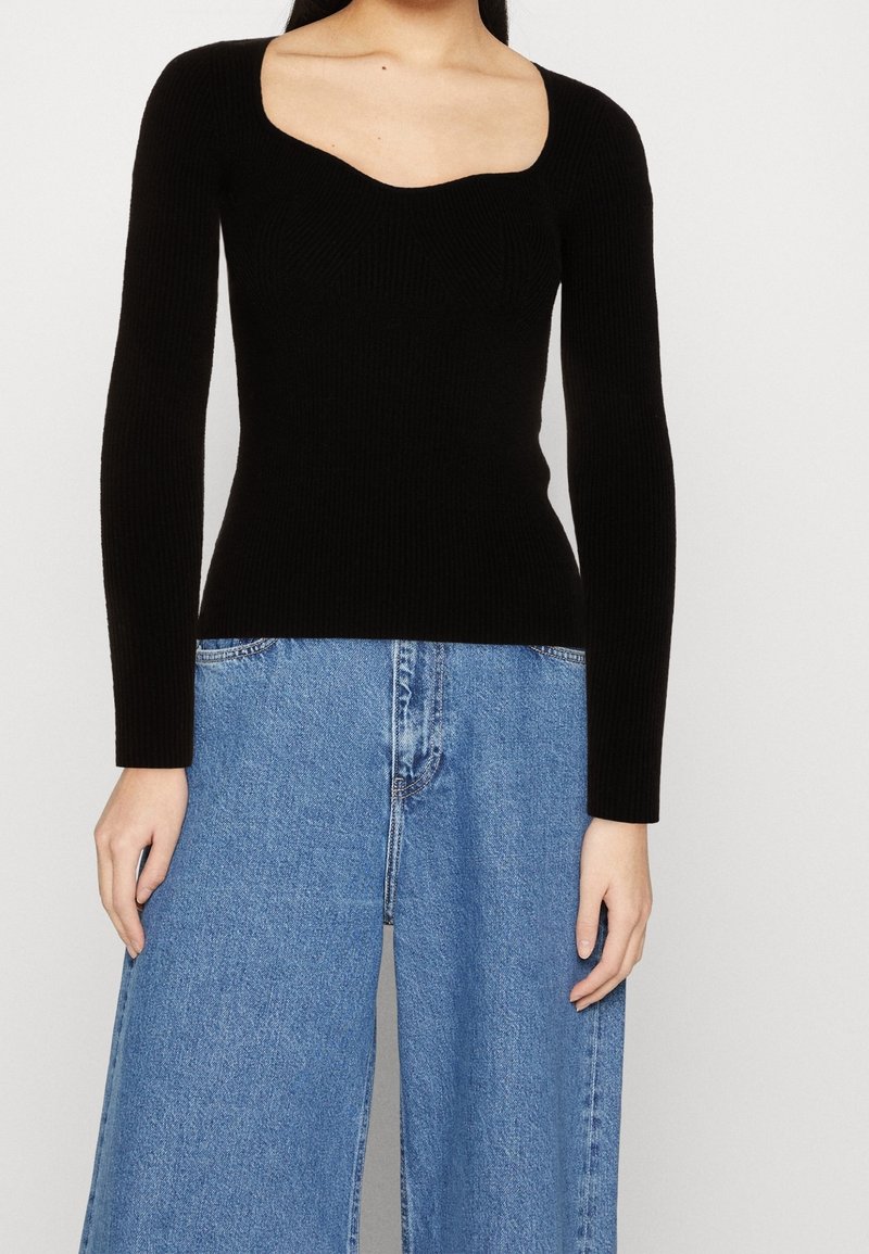 Schwarzes, geripptes Langarmoberteil mit Quadrat-Ausschnitt und taillierter Silhouette, kombiniert mit weit geschnittenen blauen Jeans aus Denim mit verwaschener Textur.