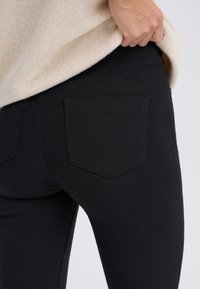 Fekete farmernadrág, testhezálló szabással, egy hátsó zsebbel és finom varrási részletekkel az derékpánton és a varratokon.
