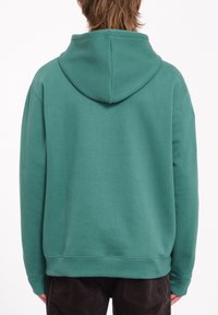Sudadera con capucha verde hecha de un material suave. Presenta un corte holgado, mangas largas y puños y dobladillo acanalados. Diseño liso.