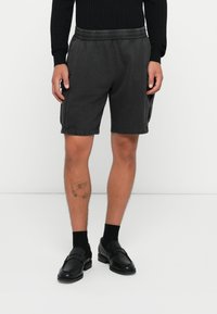 Mørkegrå afslappede shorts med elastisk talje og sidelommer, lavet af blødt stof. Bæres med sorte loafers og sokker.