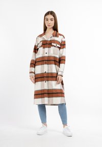 Abito camicia con bottoni in motivo plaid, caratterizzato da strisce arancioni, marroni e bianche. Realizzato in un tessuto morbido, presenta due tasche sul petto e un colletto.