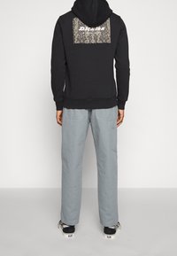 Felpa nera con cappuccio, con una toppa a stampa di serpente e logo bianco sul retro, abbinata a pantaloni cargo grigi chiari e sneakers con motivo.