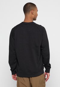 Svart crewneck-tröja med raglanärmar, mjuk textur och ribbade muddar. Har en enkel design utan synliga logotyper eller mönster.