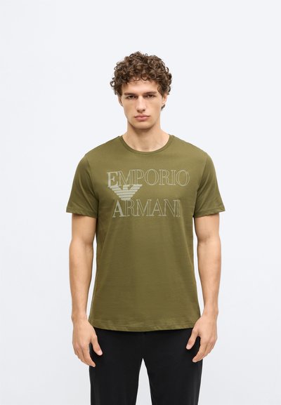 Olivzaļš T-krekls no mīksta auduma, kas ir ar drosmīgu viegli pelēku uzrakstu "Emporio Armani" uz krūtīm, ar īsām piedurknēm un apaļu kakla izgriezumu.