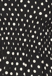 Svart tyg med vita prickar och samlad elastisk söm som skapar horisontella texturerade band.