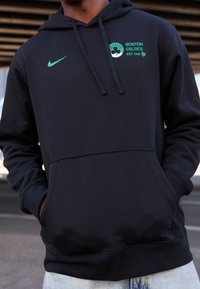 Sweat à capuche noir avec une poche avant, arborant un logo Nike vert et la marque des Boston Celtics. Confectionné en tissu doux, il est doté d'une capuche avec cordon de serrage.