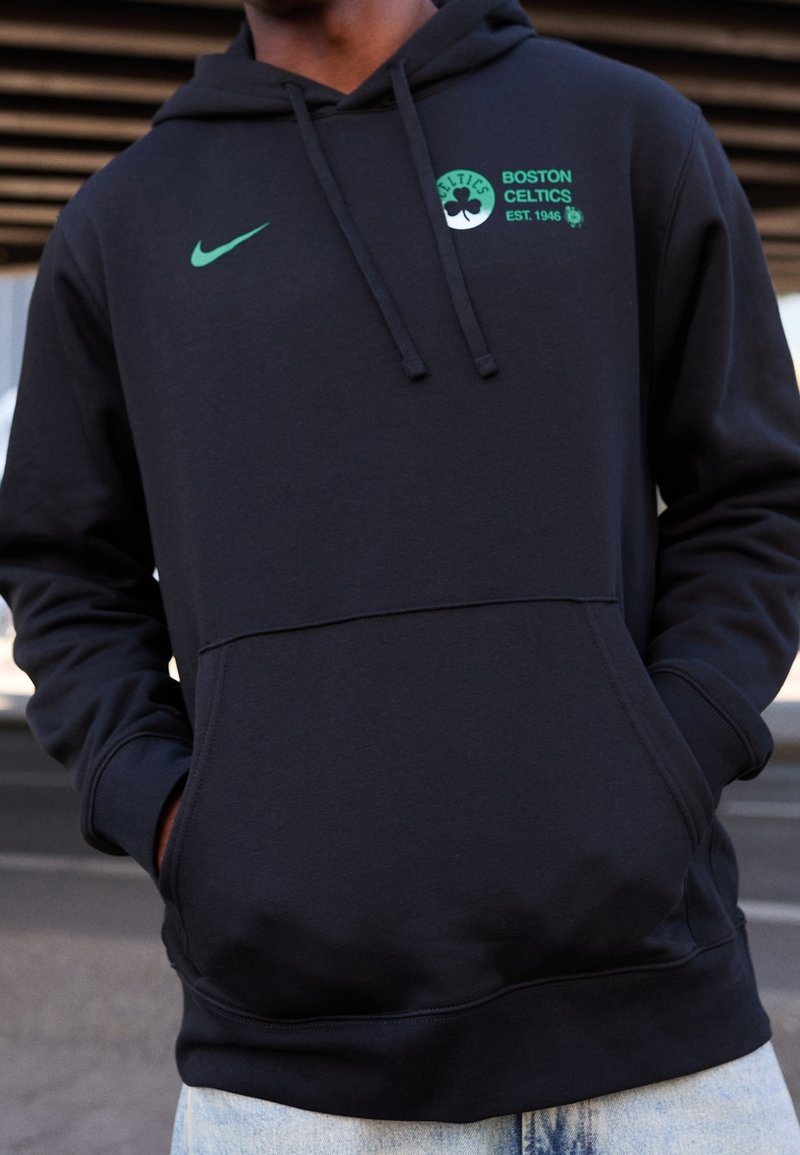 Sweat à capuche noir avec une poche avant, arborant un logo Nike vert et la marque des Boston Celtics. Confectionné en tissu doux, il est doté d'une capuche avec cordon de serrage.