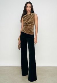 Bársonyos, ujjatlan felső gazdag barna színben, drapírozott kialakítással, melyet magas derékú, fekete bársonyos, bő szárú nadrággal párosítottak. Kiegészítve egy texturált táskával.