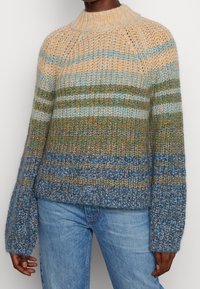 Sweter robiony na drutach z poziomymi paskami w odcieniach beżu, zieleni i niebieskiego, z wysokim dekoltem i szerokimi, ściągającymi rękawami.