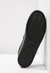 Svarta sneakers med en texturerad gummisula, som har ett fiskbensmönster och vita sidostråkar. Det övre materialet verkar vara slätt.