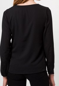 Blusa nera a maniche lunghe con scollatura rotonda, texture liscia e polsini aderenti. Presenta un design minimalista senza motivi o accenti visibili.