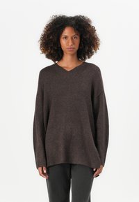 Maglione brown oversize con scollo a V e maniche lunghe. Morbido al tatto con orlo a coste, abbinato a pantaloni grigio scuro.