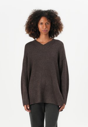 Brauner übergroßer Pullover mit V-Ausschnitt und langen Ärmeln. Weicher Stoff mit geripptem Saum, kombiniert mit dunkelgrauen Hosen.
