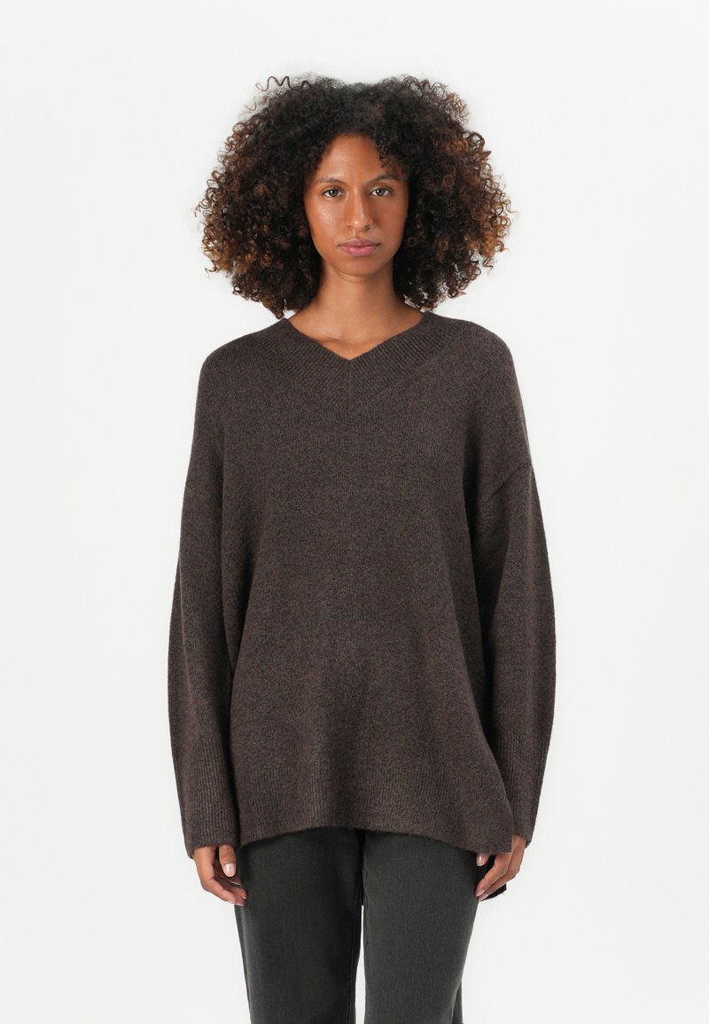 Maglione brown oversize con scollo a V e maniche lunghe. Morbido al tatto con orlo a coste, abbinato a pantaloni grigio scuro.