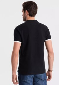 Černé polo tričko s bílými detaily na límci a rukávech. Vyrobeno z hladké tkaniny, s klasickým střihem a krátkými rukávy.