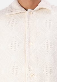 Beige színű, textúrált kardigán geometrikus kötött mintával, gallérral és elülső három gombbal. Puha, szőtt anyag.