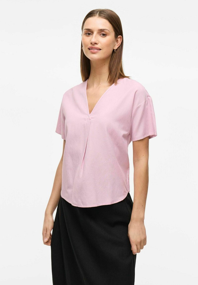 Kortärmad V-ringad rosa blus i lätt tyg med avslappnad passform, med en central veckning och rundad nederkant.