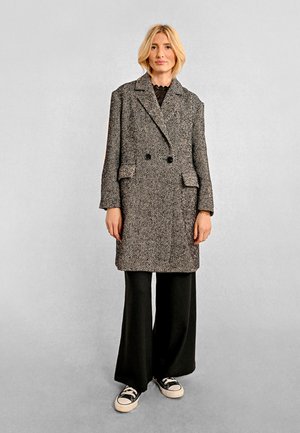 Cappotto doppiopetto a motivo pied de poule in grigio e nero, in tessuto testurizzato, con ampi revers a punta e tasche a toppa, abbinato a pantaloni a gamba larga.
