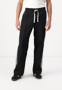 Black athletic pants with a drawstring waist, featuring white side stripes and a lightweight fabric. Straight-leg design with pockets.