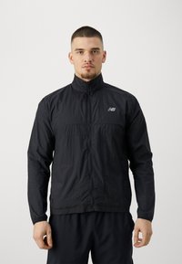 Veste légère noire avec un col montant, fermeture éclair devant et logo New Balance. Présente une finition texturée et un design pratique.