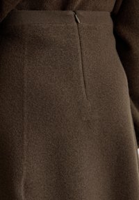 Close-up van een bruine wollen rok met een centrale achterrits bij een persoon die een bijpassende bruine top draagt.