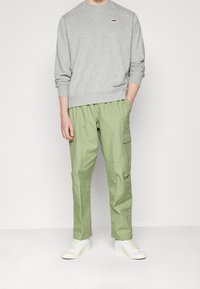 Grå sweatshirt med rund halsringning och liten logotyp, kombinerad med ljusgröna cargobyxor med sidofickor, bärs med vita sneakers.