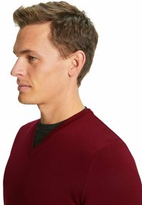 Burgunderfarbener V-Ausschnitt-Pullover aus glattem Strickstoff mit figurnahem Schnitt, an dem eine schwarze Innenschicht am Ausschnitt sichtbar ist.