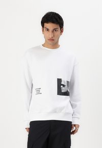 Hvit sweatshirt laget av bomullsblanding, med svart grafisk trykk og tekst på forsiden. Avslappet passform med ribbestrikkede mansjetter og hem.